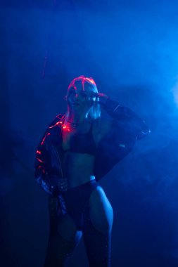 Bir dansçı, sisli bir ortamda canlı mavi ve kırmızı ışıklarla çevrili anlamlı hareketler sergiler..