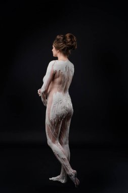 Bir model zarif poz verir, yaratıcı vücut boyalarıyla süslenir, karanlık bir stüdyo ortamında sanatsal ifadeler sergiler..