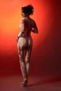Stüdyoda kırmızı neon ışıkla aydınlatılırken beyaz alçıyla kaplanmış genç çıplak kadın modelinin tüm vücut arkası görünümü
