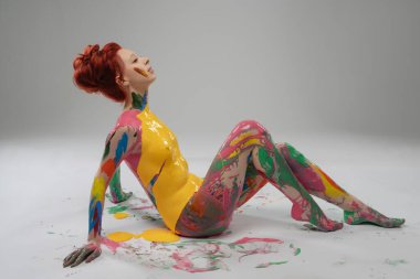 Bir kadın renkli vücut boyalarıyla kaplıyken zarif poz verir, sanatsal yanını sergiler ve yaratıcı bir ortamda güzelliği kutlar..