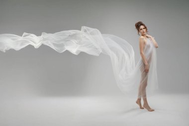 Kendine güvenen bir kadın zarif bir kumaş içinde minimalist bir ortamda güzelliğini ve zarafetini sergiliyor. İfadesi gücü ve özgüveni yansıtıyor..