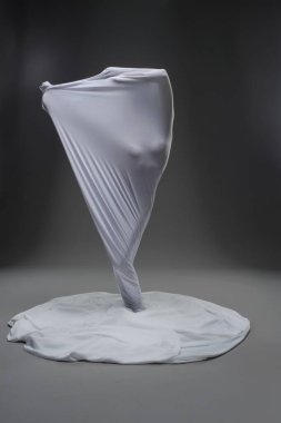 Sanatsal bir ortamda, gizli bir figür, hareket ve yaratıcılık gösteren eşsiz bir beyaz kumaş spirali sergiliyor..