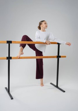 Stüdyoda bale barlarında poz veren genç bir kız dans yeteneğini ve bağlılığını sergiliyor..