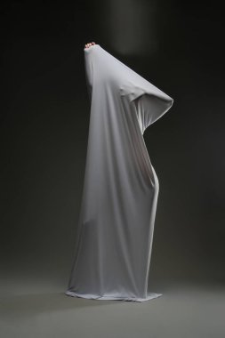 Bir kadın espriyle güzelliğini sergilerken yumuşak, katıksız bir kumaşla koyu bir arka plana sarılmış..