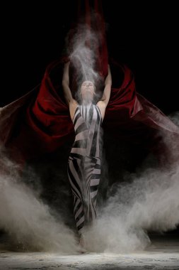 A dancer in striking black and white attire displays a powerful pose, enveloped in swirling mist and vibrant red fabric. clipart