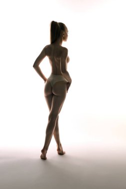 Bir kadın zarif bir şekilde poz veriyor, siluetini parlak beyaz bir arkaplanda sergiliyor..