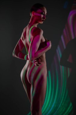 Bir kadın zarif bir şekilde duruyor, canlı ışık yansımaları ile aydınlatılıyor, sanatsal bir gösteride büyüleyici gölgeler ve renkler yaratıyor..