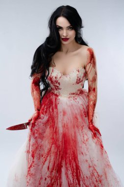 Bir gelin cüretkar bir şekilde duruyor, gelinliği kan içinde, elinde bir bıçakla, vahşi ve rahatsız edici bir güzellik yayıyor..