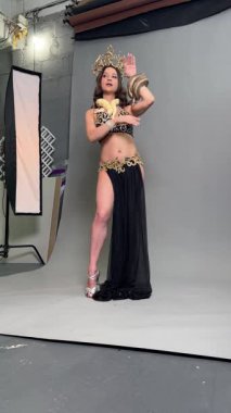 Bir kadın göbek dansını zarafetle sergiliyor, stüdyo ortamında güzel bir kostüm giyiyor..