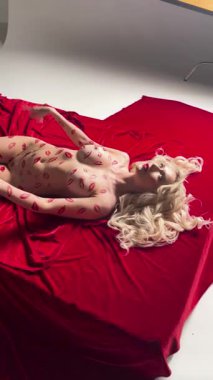 Büyüleyici bir güzellik gösterisi. Bir kadın canlı kırmızı kumaş üzerinde üstsüz poz veriyor. Vücut sanatı ve şehvetli bir aura sergiliyor..