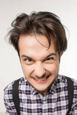 A young man with messy hair and suspenders exhibits a fierce, playful expression. The background is neutral, emphasizing his vibrant demeanor. clipart