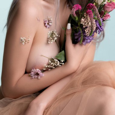 Bir insan renkli çiçekleri kucaklarken yumuşak bir zemine nazikçe oturarak sakin ve sanatsal bir atmosfer yaratıyor..