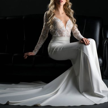 Dantelli, güzel beyaz bir elbise giyen bir gelin zarif, siyah bir kanepede poz verir zarafetini ve tarzını sergiler..