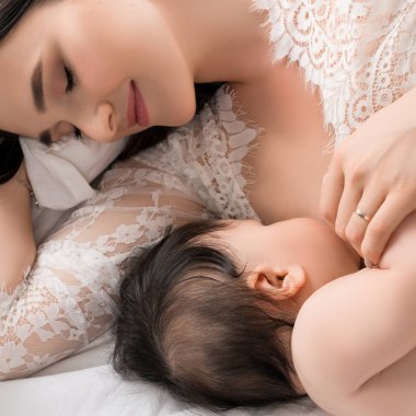 Bir anne bebeğini emzirirken yumuşak bir yatakta uzanıp sıcak ve samimi bir an yaratarak bağ kurar..