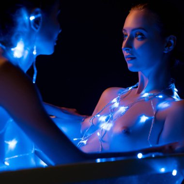 Parlayan mavi ışıklara sarılmış iki figür huzurlu ve samimi bir ortam yaratıyor. Sahne, yumuşak aydınlatma altında güzellik ve sükuneti yakalar..