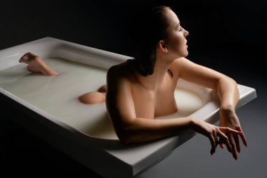 Bir kadın, sakin bir ortamda güzelliğini ve vücut sanatını sergileyerek, yumuşak ışıkla çevrili rahatlatıcı bir banyodan zevk alır..