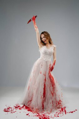 Gelin gibi giyinmiş, kana bulanmış bir kadın, başının üstünde bir katana tutuyor, çarpıcı derecede dramatik bir atmosfer yaratıyor..