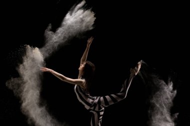 Çizgili kostümlü bir dansçı dinamik bir şekilde hareket ederken un saçıyor ve karanlık bir arkaplana karşı soyut şekiller yaratıyor..