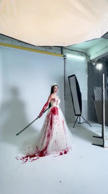 Çarpıcı bir elbisesi ve dramatik kan efektleri olan bir gelin sahne arkasında büyüleyici bir fotoğraf çekimine hazırlanıyor..