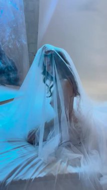 Bir kadın, sakin bir stüdyoda üstsüz poz verip sahne arkasında büyüleyici bir atmosfer yaratıyor..