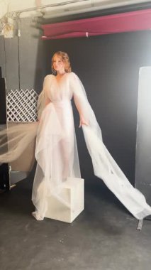 Güzel bir gelin sahne arkasına hazırlanıyor, gelinliği ve yumuşak peçesiyle zarafet ve sanatını sergiliyor..