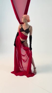 Bir kadın zarif iç çamaşırlarıyla ve yaratıcı bir sahne arkası seansı sırasında dalgalı kırmızı bir parçayla gösteriş yapar..