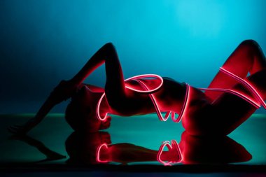 Bir kadın zarif poz verir, neon ışıklı aksanlarla süslenir, samimiyet ve zarafet gösterir. Zıt renkler büyüleyici bir atmosfer ekler..