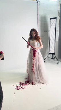 Çarpıcı bir gelinlik giymiş bir gelin dramatik bir kırmızı boya damlasıyla elinde bir kılıçla tiyatro çekimine hazırlanıyor..