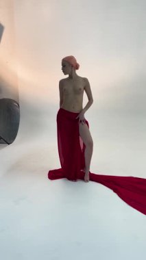 Çekici bir kadın bir güzellik etkinliğinde sahne arkasında kırmızı bir elbiseyle zarifçe poz verir. Atmosfer sanatsal ve canlı..