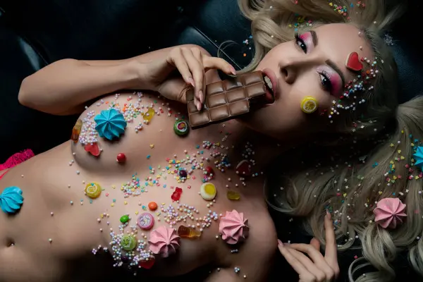 Renkli vücut sanatına sahip bir kadın çikolatanın tadını çıkartıyor, canlı yaratıcılığını şekerlerle gösteriyor..