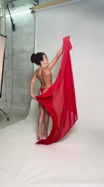 Bir kadın, dansını geliştirmek ve yaratıcılığını göstermek için kırmızı kumaş kullanarak stüdyoda üstsüz poz verir..