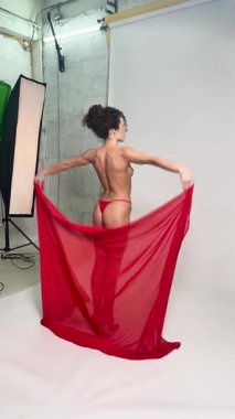 Bir kadın stüdyoda zarif bir şekilde poz veriyor, canlı kırmızı kumaşla dans ediyor, sanatsal ifadesini vurguluyor..