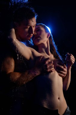 Düşen suyun altında, düşük ışıkta duran bir çift, duygusal bir atmosfer yaratarak, samimi bir anı paylaşır..