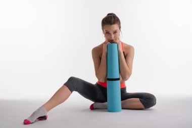 Bir kadın stüdyo zemininde yoga minderiyle dinleniyor, atletizmini sergiliyor ve bir spor sahasına odaklanıyor..