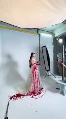 Gelin gibi giyinmiş bir kadın sahne arkasında fotoğraf çekimine hazırlanırken dramatik kan efektleri sergiliyor..