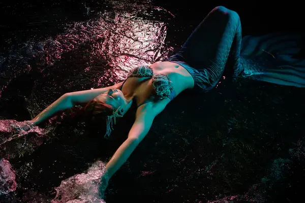 Denizkızı kılığında bir kadın, gece boyunca suda yatarken vücut sanatını sergiliyor..