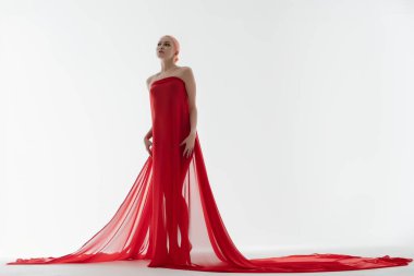 Güzel bir kadın, minimalist bir ortamda yumuşak, ruhani bir ışıkla biçimlendirilmiş, dalgalı kırmızı bir elbisenin içinde güvenle duruyor..