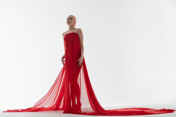 Красивая женщина уверенно стоит в темной красной одежде, стилизованной с мягким, эфирным светом в минималистской обстановке.