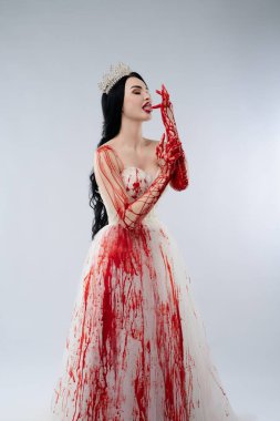 Kana bulanmış bir gelinlik giymiş bir gelin, hem güzelliği hem de tehdidi çarpıcı bir kontrastla somutlaştıran bir bıçak tutar..