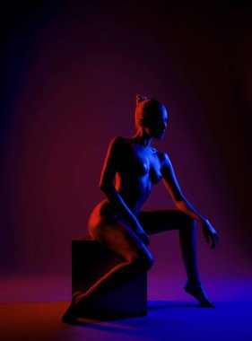 Çarpıcı silüetine sahip bir model, çarpıcı mor ve kırmızı ışıklarla aydınlatılmış bir küp üzerinde diz çöker ve uzayda büyüleyici bir kontrastlık yaratır..