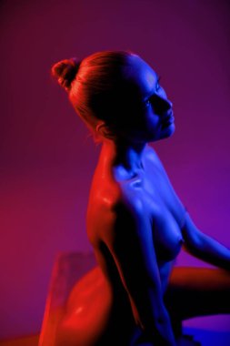 Bir model zarif poz verir, canlı mavi ve kırmızı vücut boyasını cesur bir arka plana karşı sergiler, sanatsal ifade ve yaratıcı ışıklandırmayı vurgular..