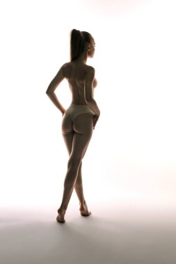 Bir kadın zarif bir şekilde poz veriyor, siluetini parlak beyaz bir arkaplanda sergiliyor..