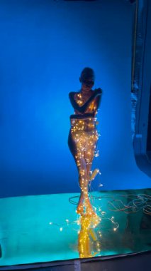 Büyüleyici bir model sahne arkasında parıldayan ışıklarla çevrili iç çamaşırlarıyla zarifçe poz verir..