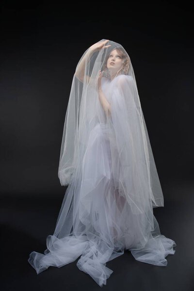 A striking woman poses gracefully in a flowing lace wedding gown, exuding beauty and a sense of enchantment.