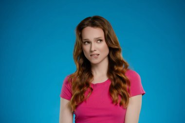 Bir kadın stüdyoda poz veriyor, benzersiz bir ifade sergiliyor. Arkaplan, portrenin genel havasını artıran parlak mavi bir renktir..