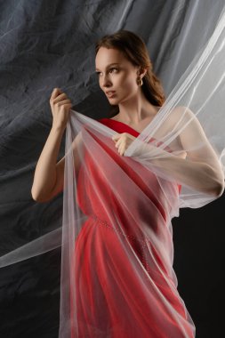 Bir stüdyo ortamında, bir kadın duruşu sergilerken etrafını sarar, derin duygu ve zarafetle doldurulmuş bir anı yakalar. İfadesi güç ve yoğunluk taşıyor..