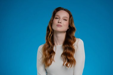 Kendine güvenen bir kadın stüdyo ortamında poz veriyor, ifadesiyle çeşitli duygular sergiliyor. Zengin mavi arka plan, doğal güzelliğini ve karizmasını arttırarak çarpıcı bir görsel yaratıyor..