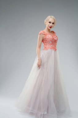 Stüdyoda, üzerinde kan lekesi olan zarif bir gelinlik olan bir kadın kendine güvenerek ayakta duruyor. Onun çarpıcı görünüşü yumuşak kumaşla çelişiyor, rahatsız edici ve büyüleyici bir görüntü yaratıyor. Şey...