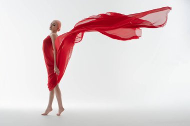 Bir kadın zarif bir şekilde poz verir, dalgalı kırmızı kumaşla örtülmüş, narin ışıklandırmalı minimalist bir ortamda güzelliği somutlaştırır..