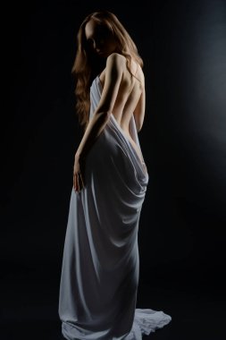 Model, minimalist bir ortamda zarafet sergiliyor, kumaşa bürünmüş ve büyüleyici bir poz veriyor..